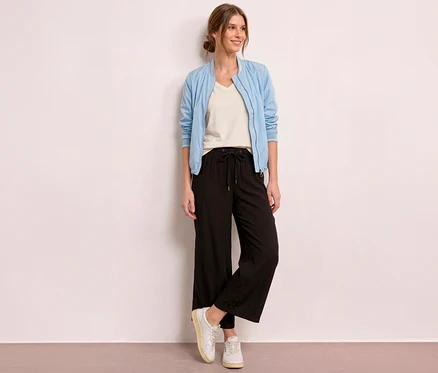 Eine lächelnde Frau steht vor einer hellen Wand und trägt eine hellblaue Bomberjacke, ein cremefarbenes T-Shirt und eine schwarze Street One 7/8-Culotte »EMMA«.