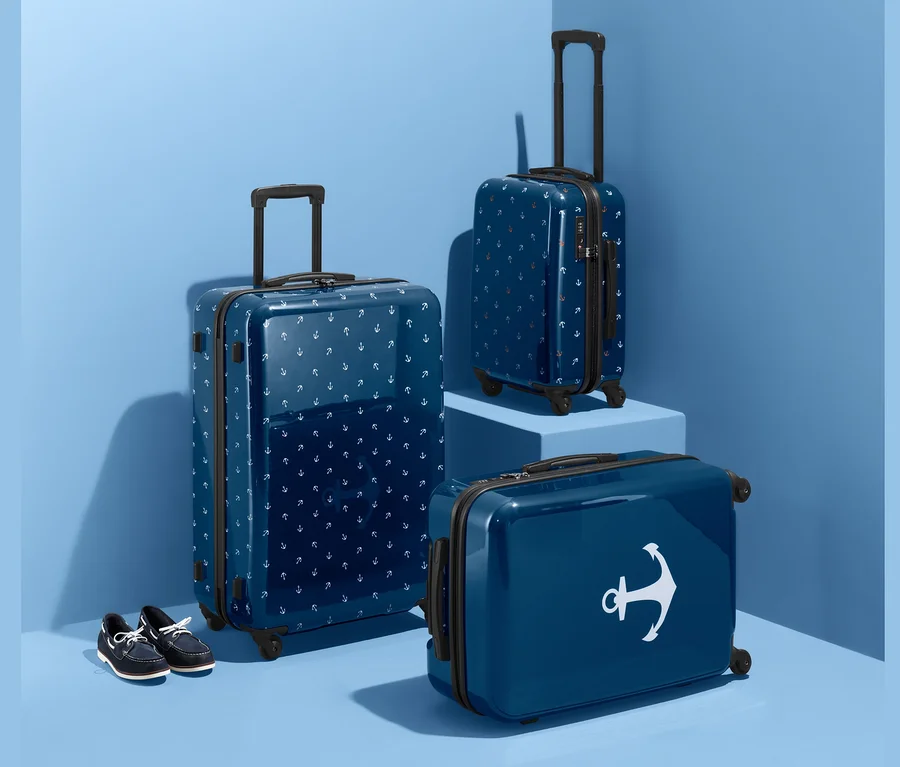 Drei blaue Hartschalen-Koffer (groß, mittel und klein) mit Anker-Muster und blaue Schuhe vor blauem Studiohintergrund.