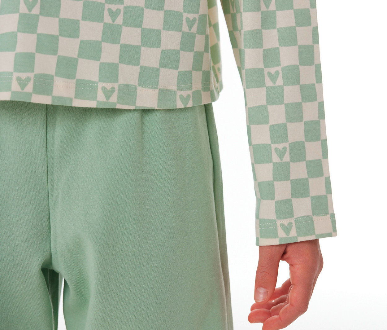 Kind trägt einen SCHIESSER Kinder-Interlock-Pyjama mit hellgrün-cremefarbenem Schachbrettmuster-Oberteil mit Herzchen und einer hellgrünen Hose.