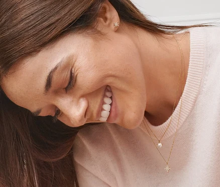 Eine lächelnde Frau trägt Gold-Ohrstecker Stern mit Zirkonia, Gold-Kette Stern mit Zirkonia und Gold-Kette mit Süßwasserzuchtperle.