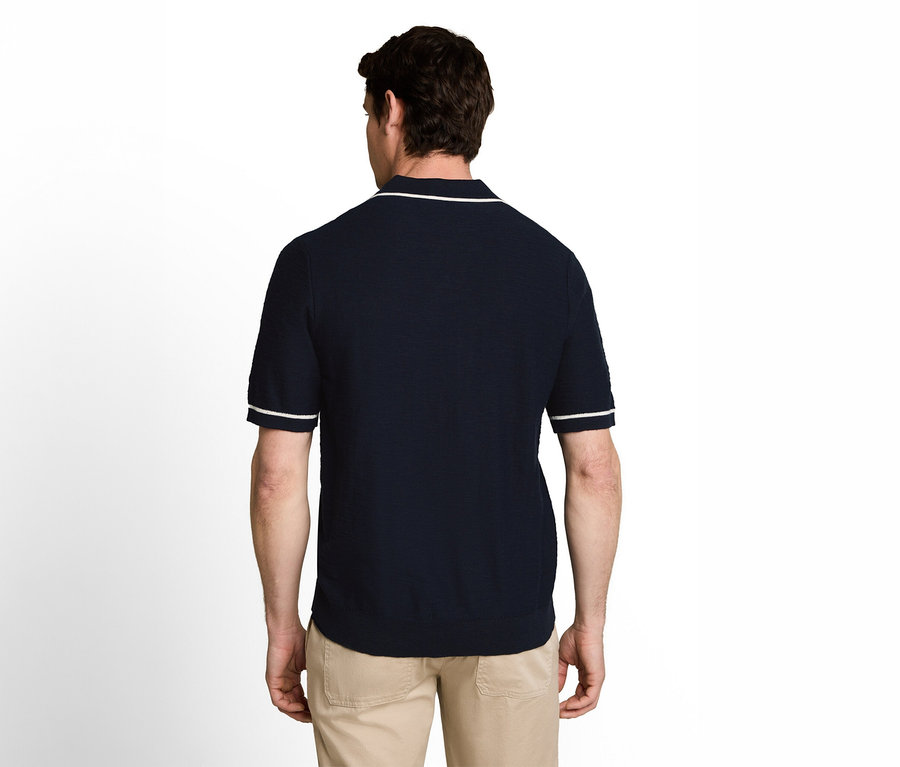 Mann von hinten gesehen, der ein dunkelblaues Poloshirt mit weißem Besatz am Kragen und an den Ärmeln sowie eine beigefarbene Hose trägt.