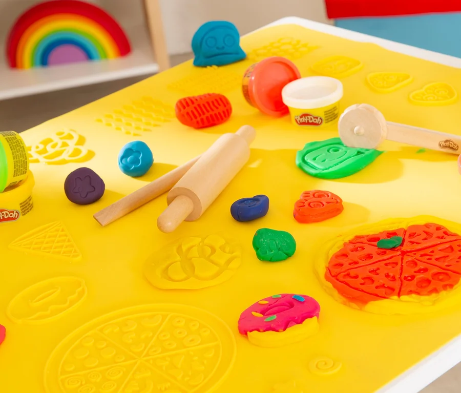 Nahaufnahme von Play-Doh und Werkzeugen auf einem gelben roba x Play-Doh Sitzgruppen-Set Tisch. Regenbogen im Hintergrund.