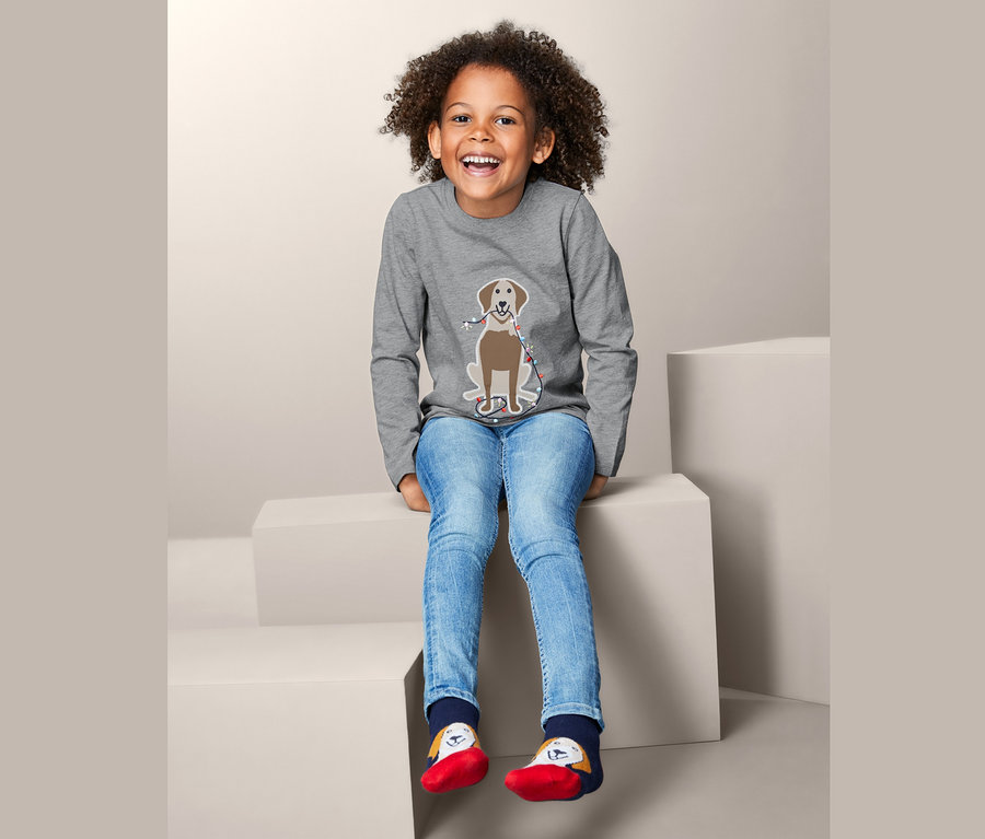 Ein Mädchen sitzt auf Stufen und trägt ein graues Langarmshirt mit Hundemotiv.