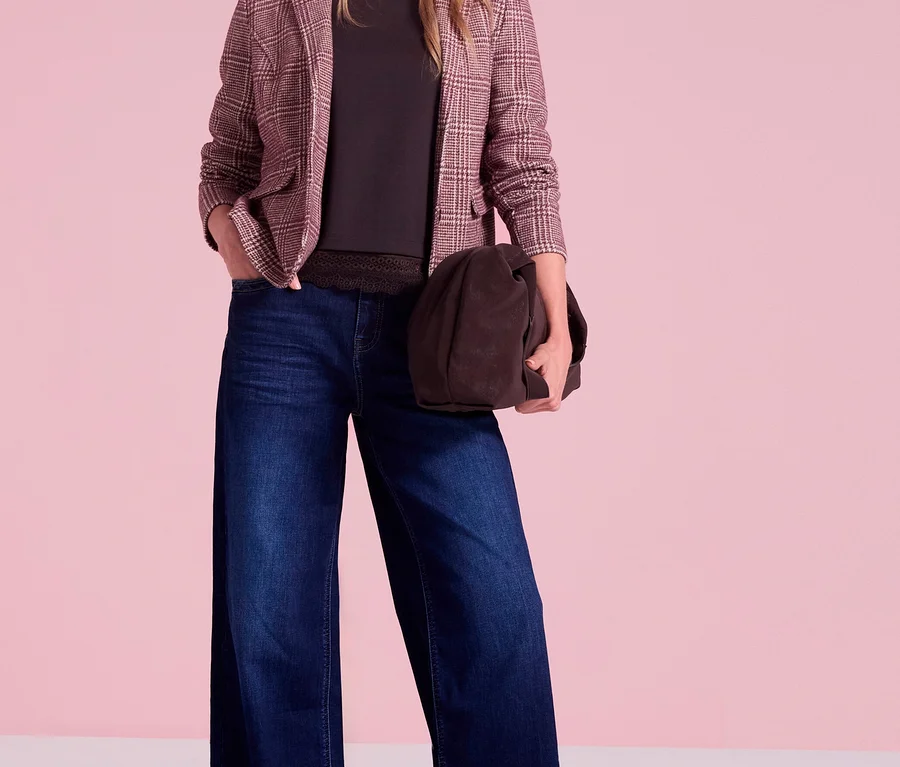 Eine Frau trägt einen karierten Street One Blazer, ein dunkles Oberteil mit Spitzenbesatz, weite Jeans und spitze Ballerinas, während sie eine braune Tasche hält.
