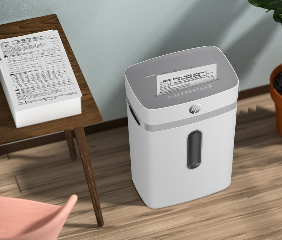 Ein Stapel Dokumente liegt auf einem Holztisch neben einem weißen HP OneShred 12CC Aktenvernichter.