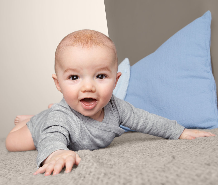 Ein Baby liegt auf dem Bauch auf einem grauen Stoff und trägt einen grauen 3er-Pack Langarmbody.