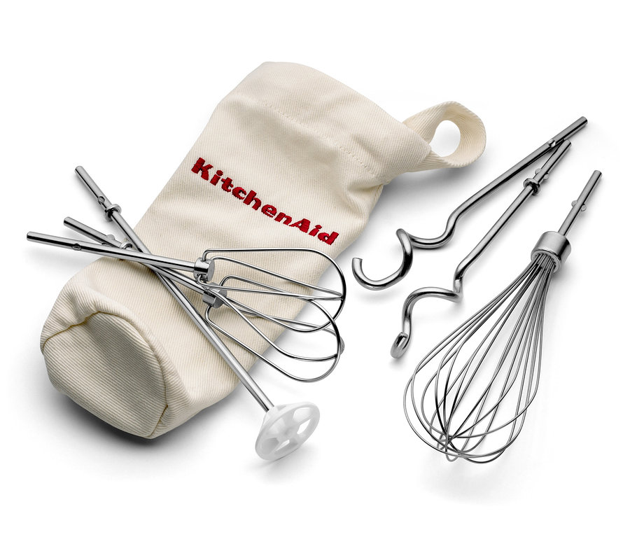Küchenmaschine Zubehör: Schneebesen, Knethaken und Schneebesen liegen neben einem beige Stoffbeutel mit KitchenAid Schriftzug. Zu sehen ist der KitchenAid-Handmixer »5KHM9212« in cremefarben.