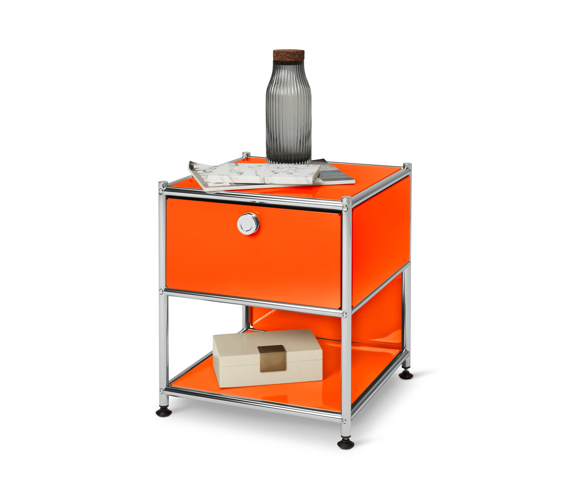 Ein orangefarbener Beistelltisch mit Schublade Metall »CN3«, darauf eine Flasche und eine Zeitung, im unteren Regal eine Schachtel.