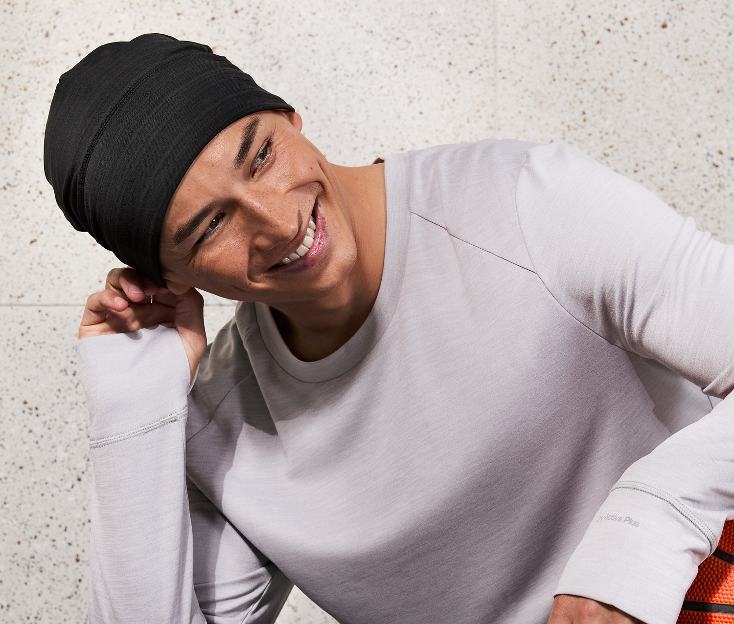 Mann mit schwarzer Funktionsmütze sitzt lächelnd und hält einen Basketball.