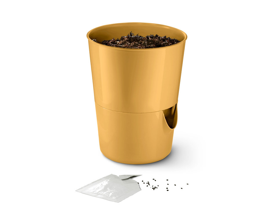 Ein gelber Kräutertopf mit Bewässerungssystem, Erde und Samen auf einem weißen Hintergrund.