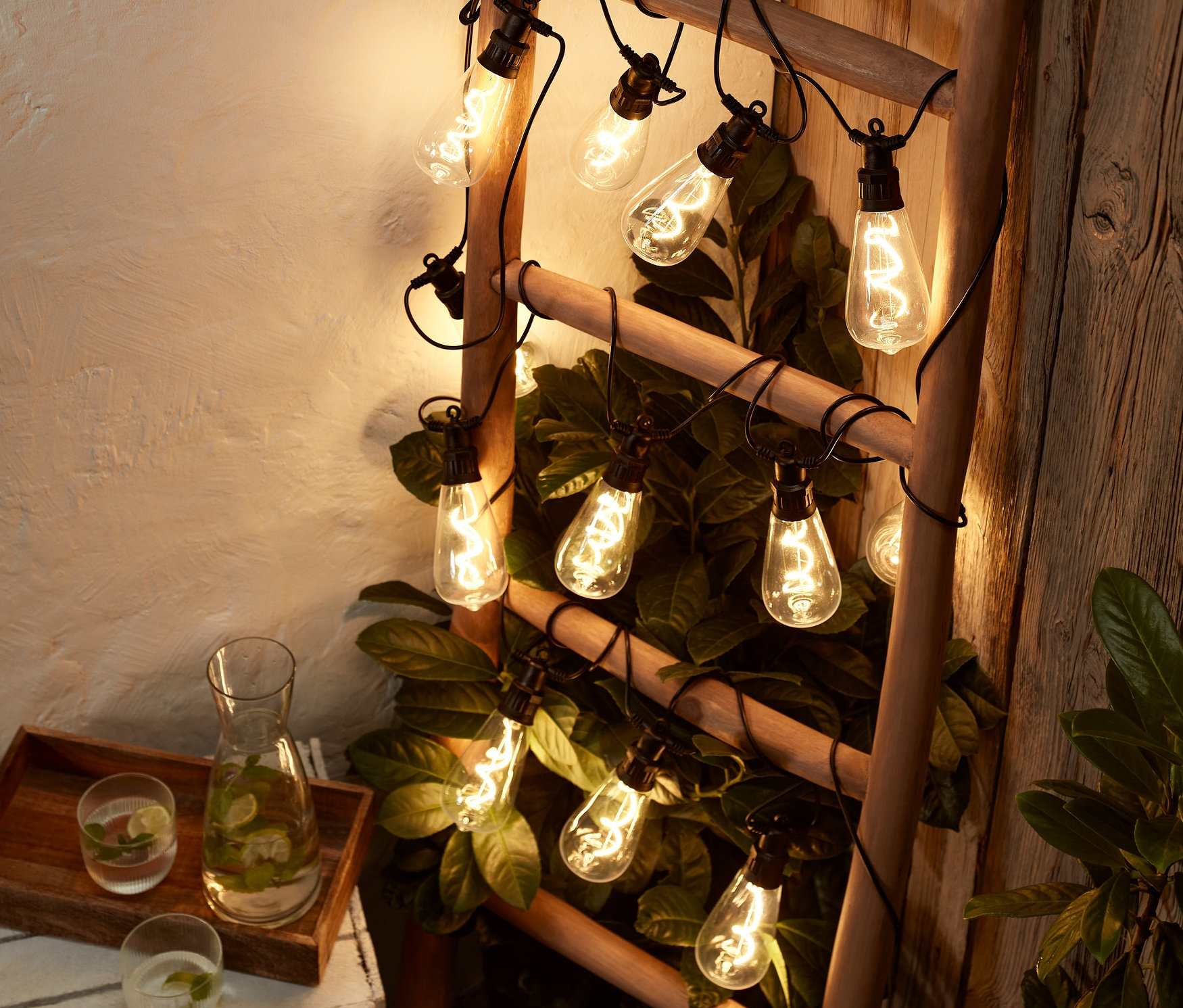 Eine Leiter ist mit einer LED-Filament-Lichterkette umwickelt, daneben ein Getränk mit Minze.