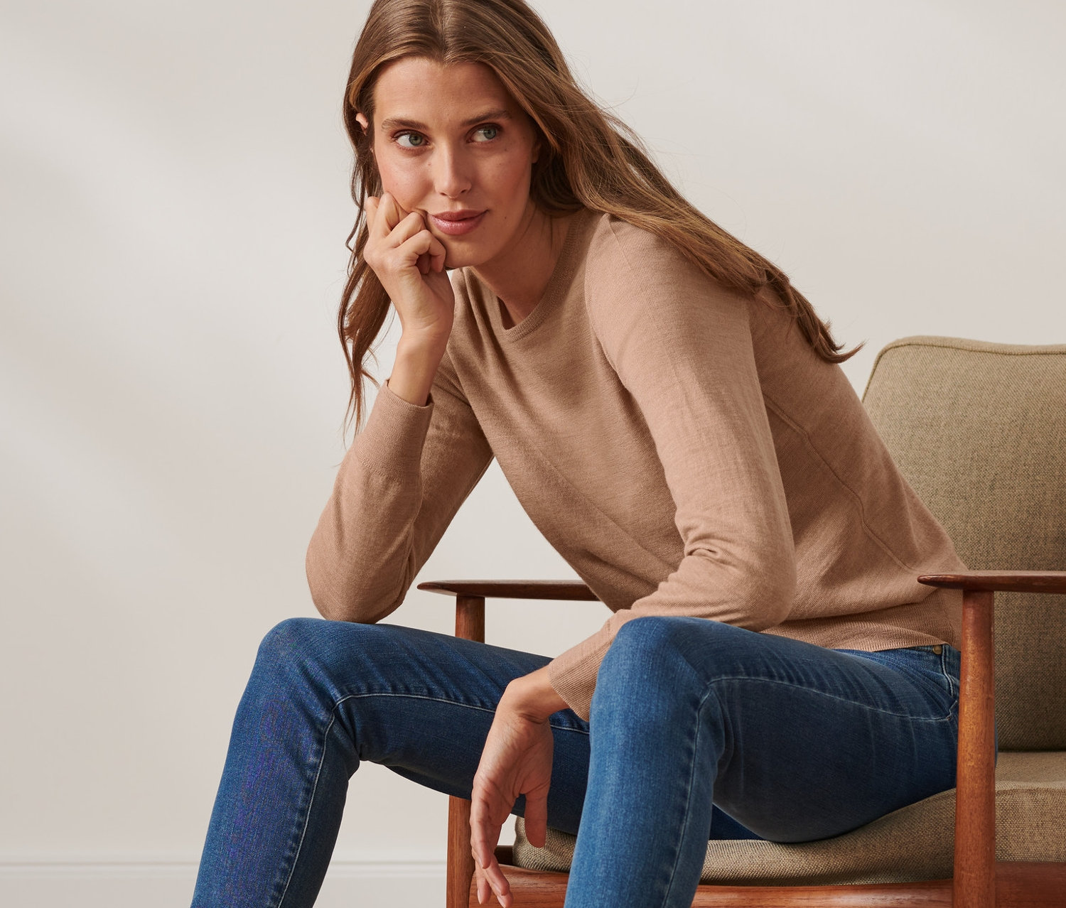 Frau sitzt im Sessel und trägt einen beige melierten Pullover aus Merinowolle.