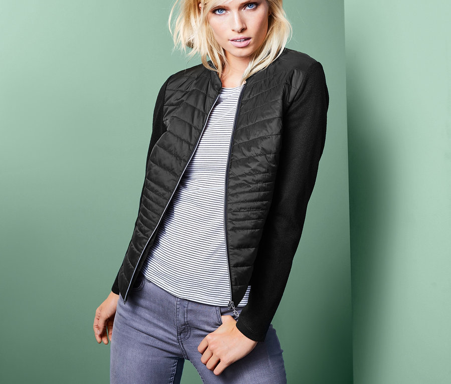 Frau posiert in Jacke im Materialmix, gestreiftem T-Shirt und Jeans.