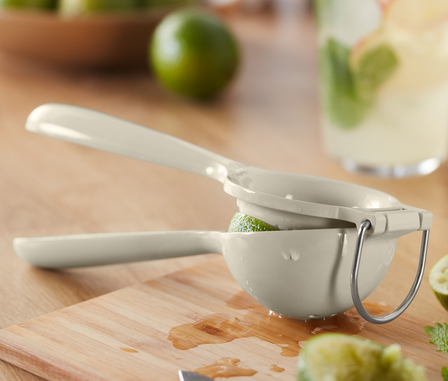 Eine Zitruspresse presst eine Limette auf einem Schneidebrett, neben einem Getränk und einer Schüssel mit Limetten.