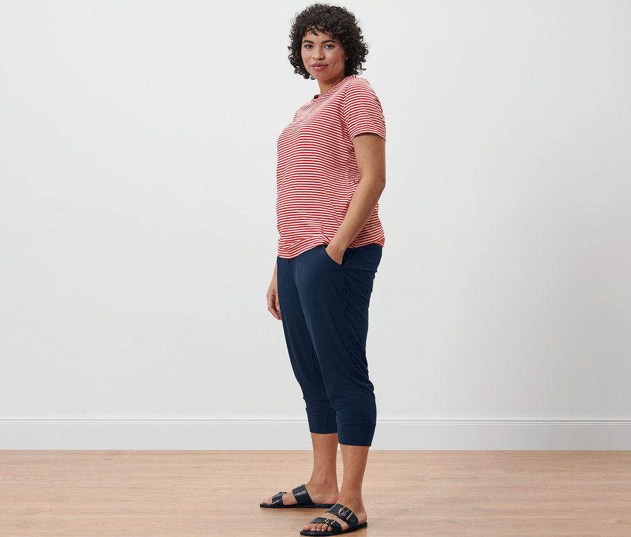 Frau in gestreiftem T-Shirt und 3/4-Jerseyhose steht seitlich.