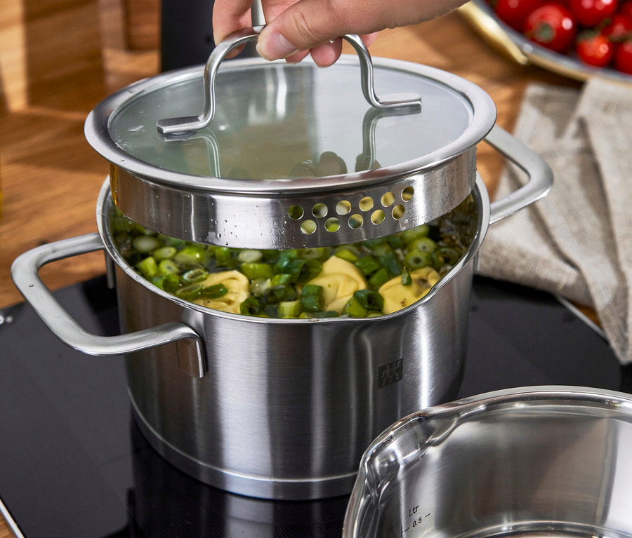 Eine Hand hält den Deckel über einem ZWILLING Trueflow Kochtopf aus Edelstahl mit Pasta und Gemüse.