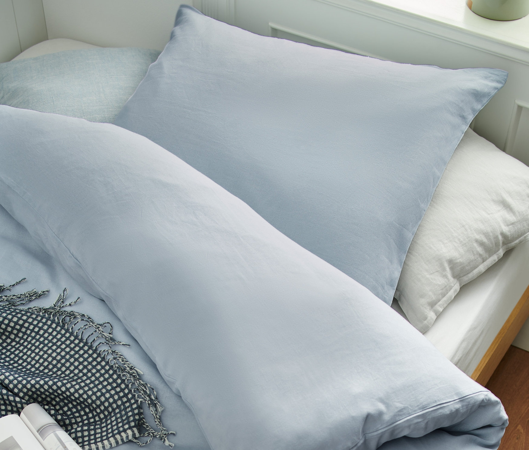 Detailansicht von blauer Leinen-Bettwäsche in verschiedenen Größen auf einem Bett mit Kissen und einer Decke.