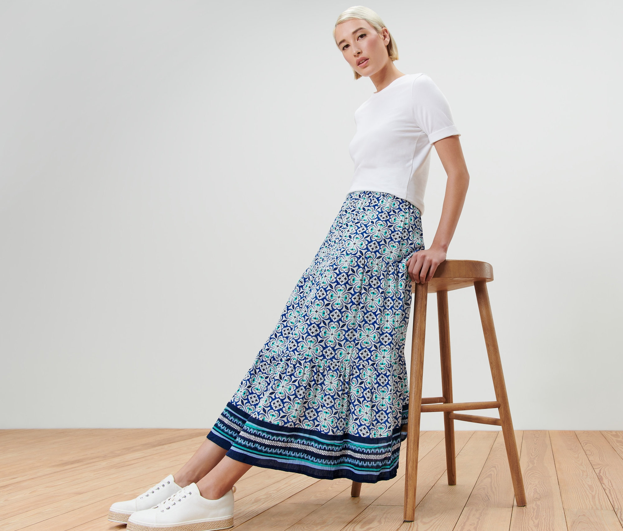 Frau sitzt seitlich auf einem Holzhocker und trägt einen Webrock mit Alloverprint.