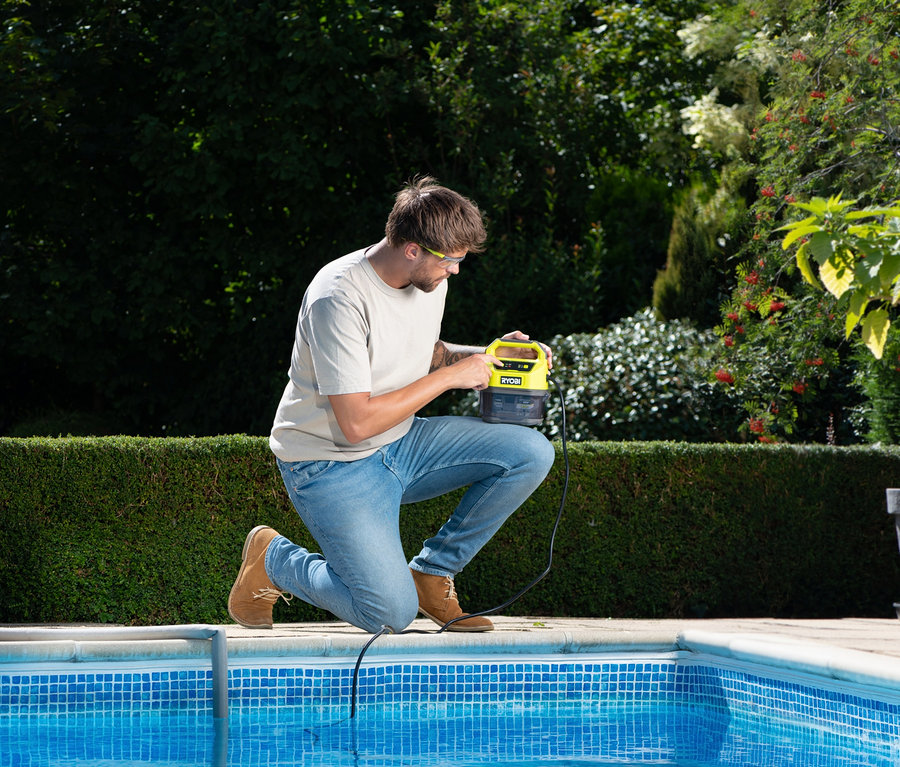 Mann kniet am Pool und hält eine RYOBI 18 V One+ Akku-Tauchpumpe.