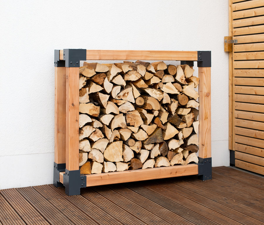 Ein Kaminholzständer, L, gefüllt mit geschnittenem Holzscheiten.