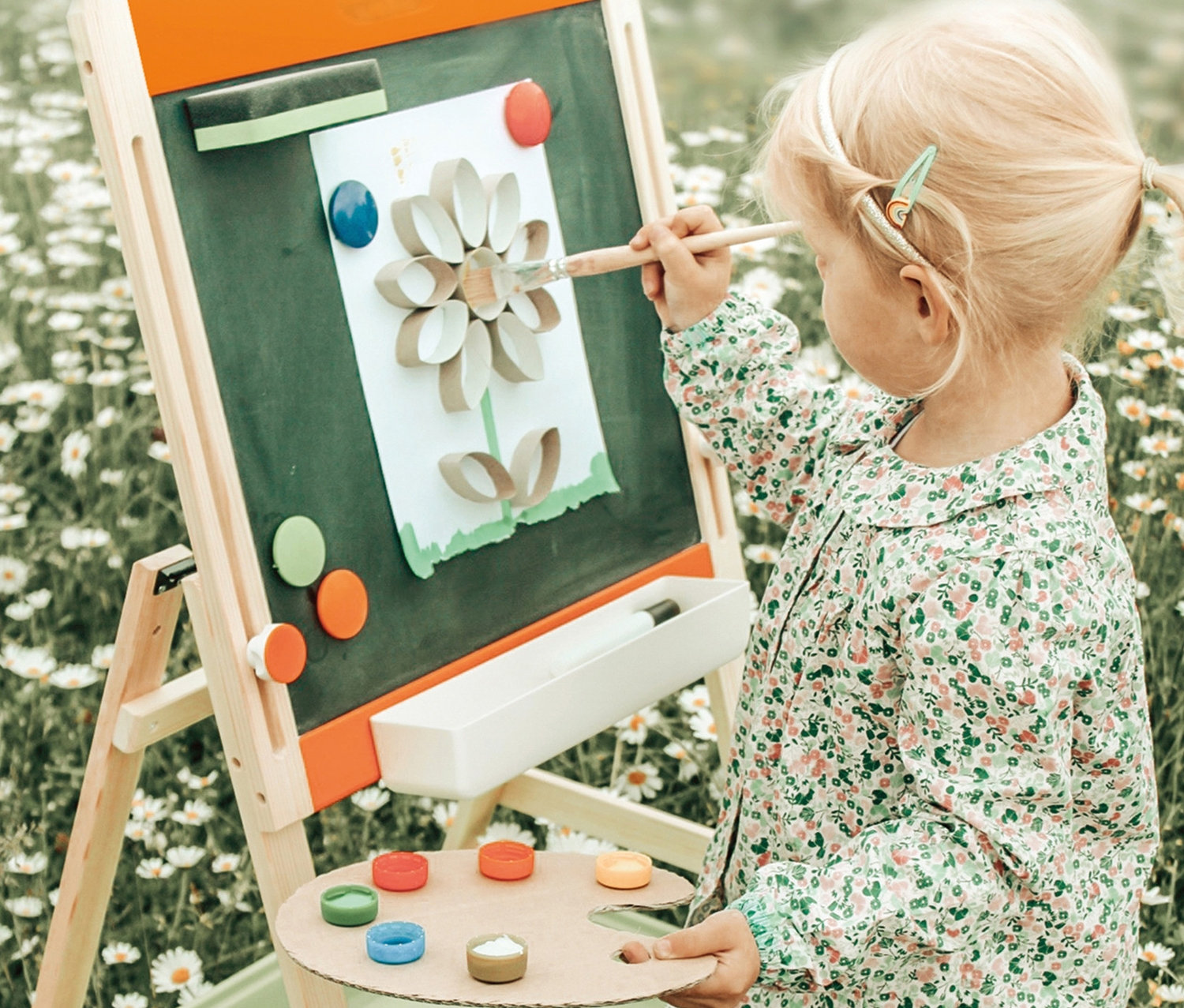 Mädchen malt Blume auf small foot Kreide-und Magnettafel auf Wiese.