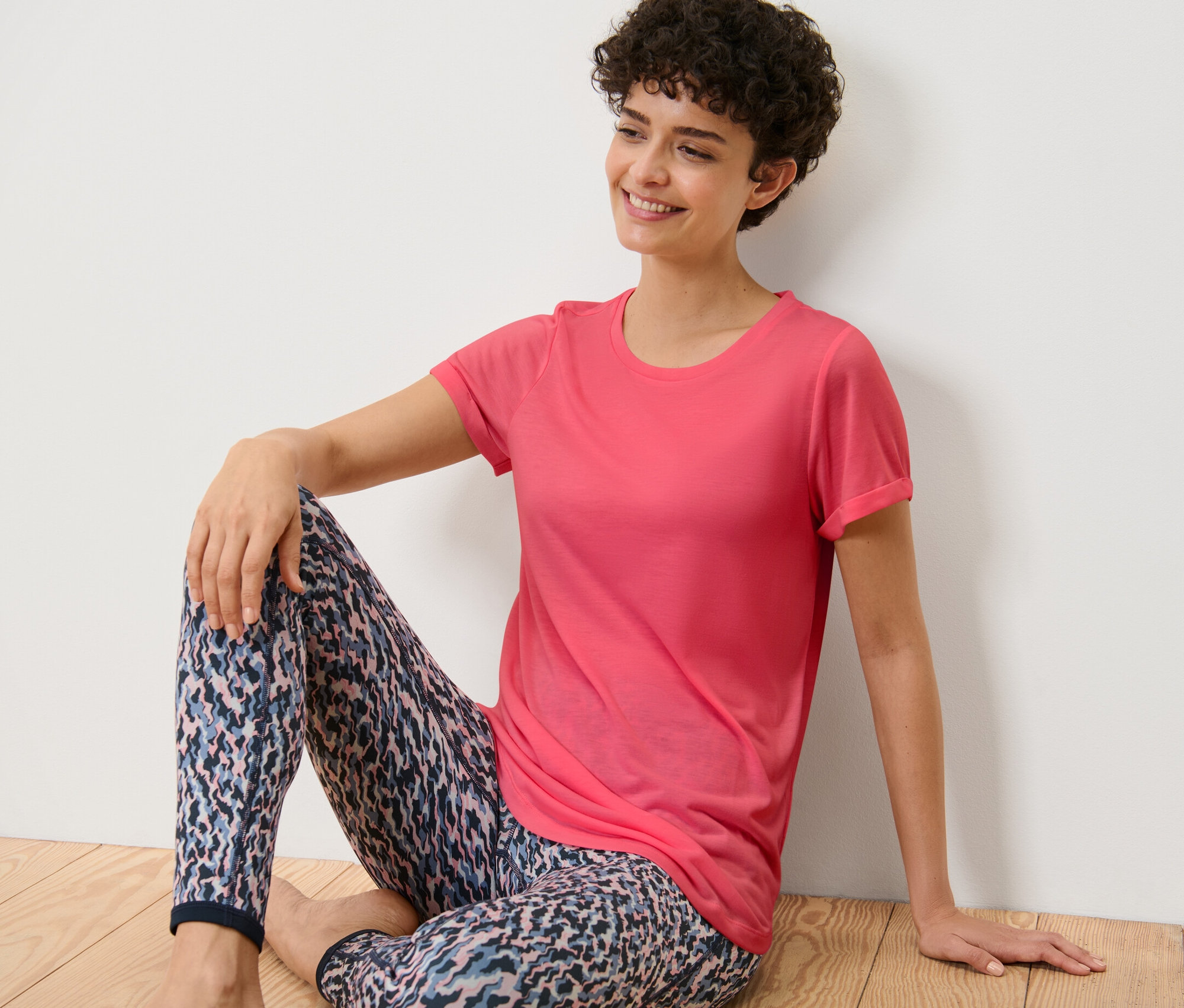 Frau sitzt auf dem Boden und trägt ein pinkes Longshirt.