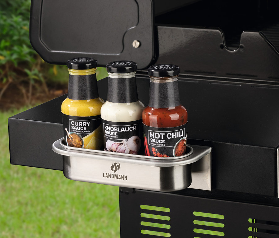 Drei Soßenflaschen in einem Metallhalter an einem Grill.