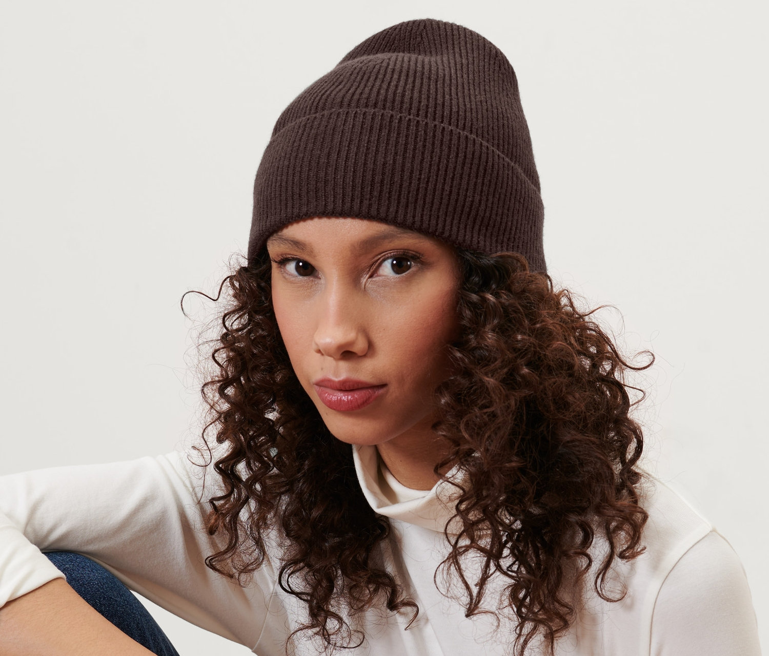 Frau sitzt und trägt eine braune Strickmütze.