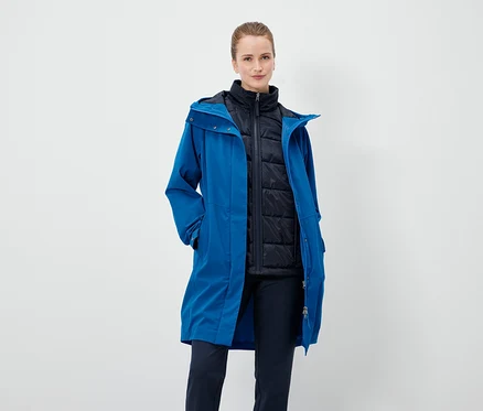 Eine Frau trägt einen blauen Mantel und eine schwarze Weste.