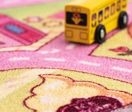 Detailaufnahme eines Kinder-Spielteppichs »Sweet City« mit einem gelben Spielzeugbus.