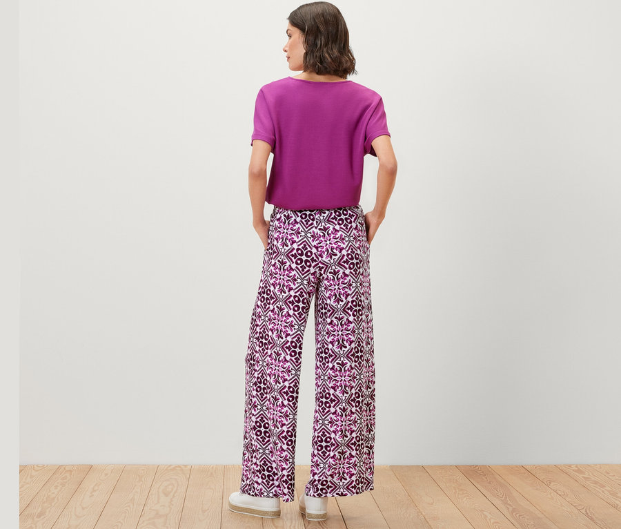 Frau trägt eine bedruckte Palazzohose in Berry-Farbe und ein lila T-Shirt.