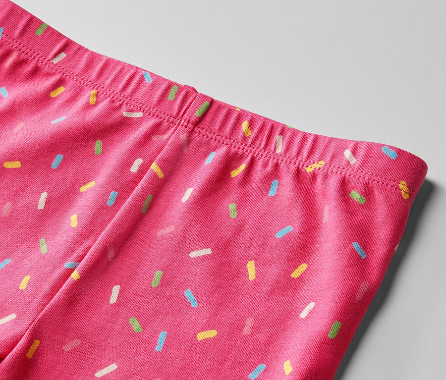 Detailansicht vom Bund einer pinken Leggings, bedruckt mit bunten Streuseln. 2 Kinder-Radler-Leggings, pink und gelb.