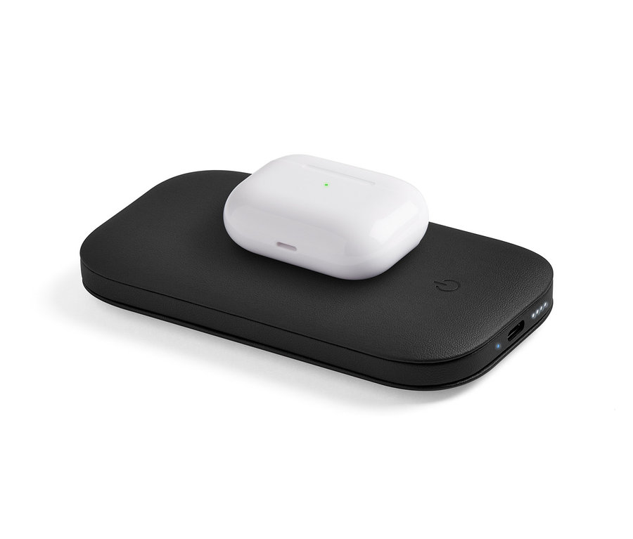 Ein weißes Kopfhörergehäuse liegt auf einer schwarzen, kabellosen Powerbank. Auf der schwarzen Lexon »SOFTPOWER«.