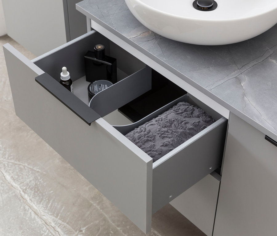 Offene Schublade mit Kosmetika und Handtuch unter einem Waschbecken. Im Unterschrank ist ein »Alessio« Waschtisch.