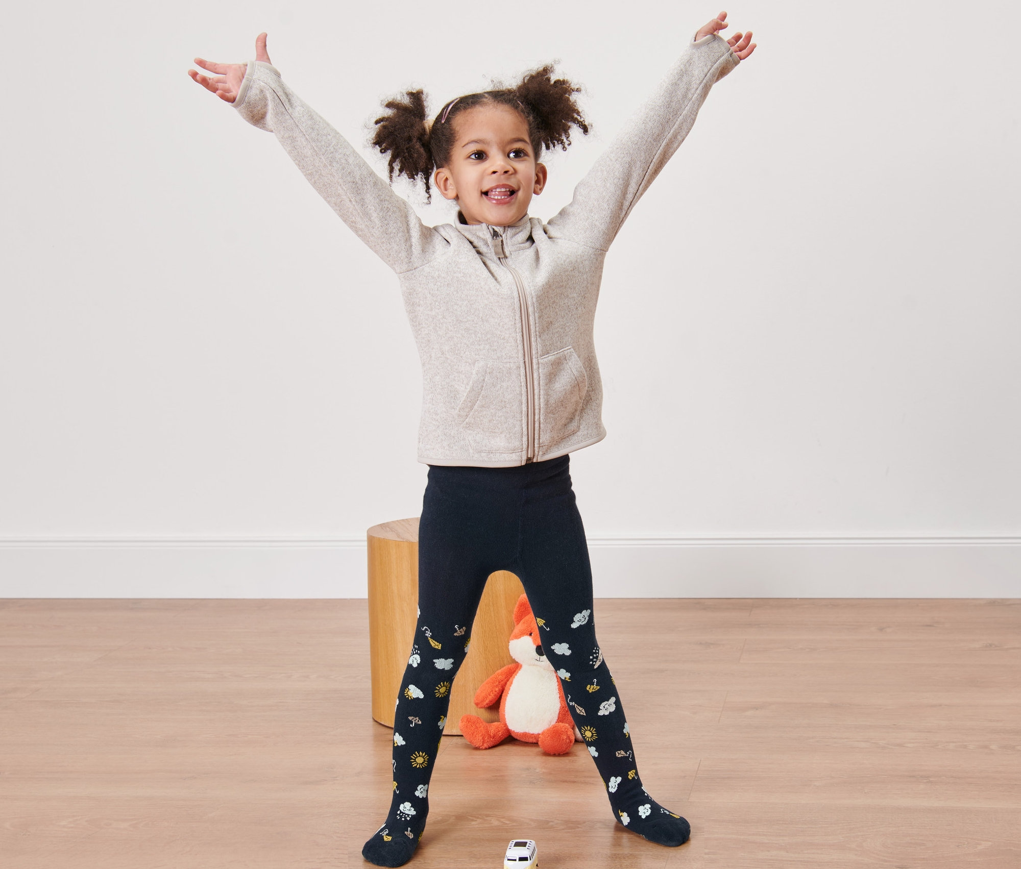 Lächelndes Mädchen steht mit ausgestreckten Armen und trägt blaue Strumpfhosen.