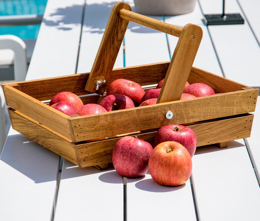 Rote Äpfel im hölzernen Erntekorb auf einem weißen Tisch.