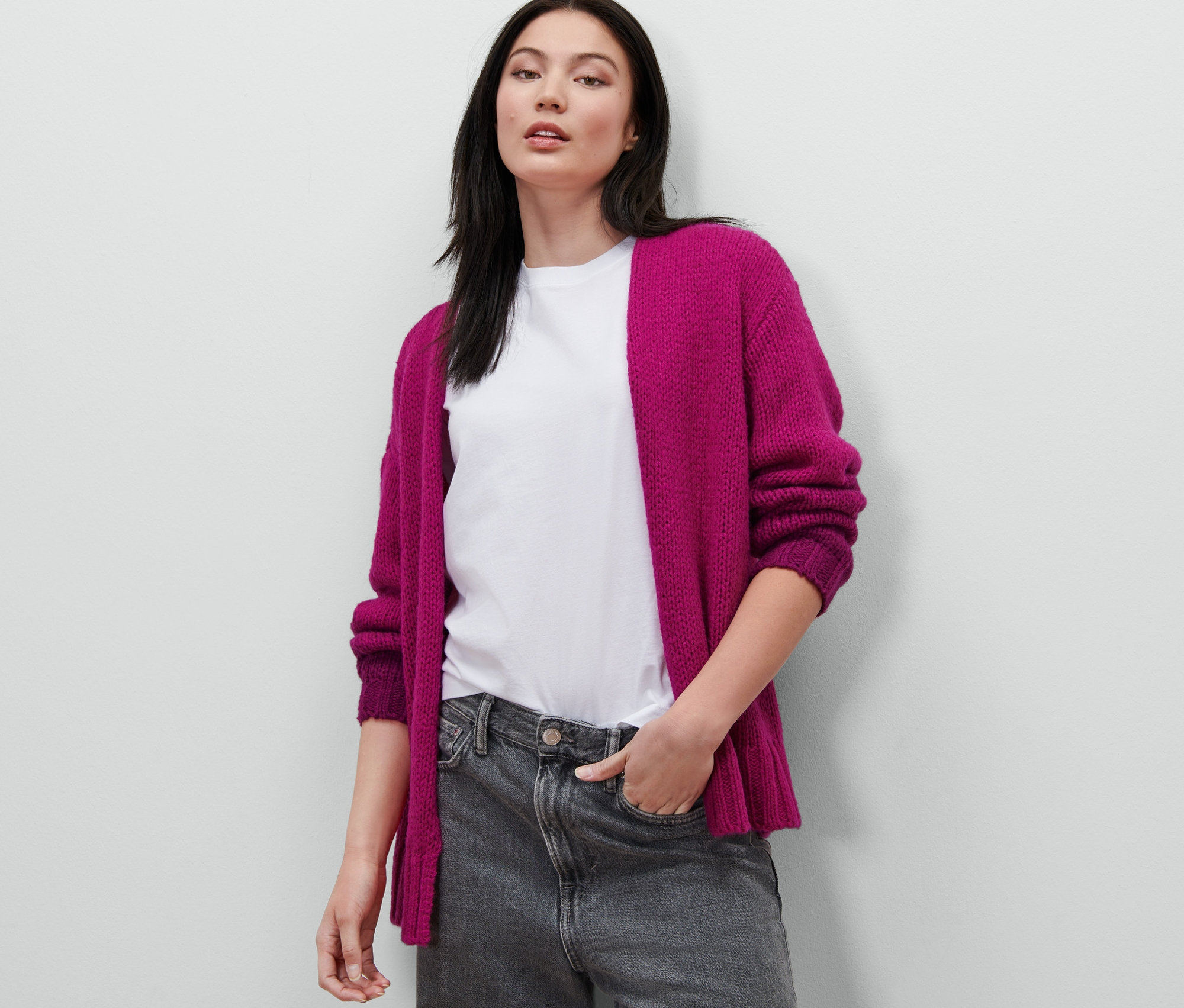 Eine Frau posiert in einem Oversized-Cardigan mit Wolle, einem weißen T-Shirt und grauen Jeans.