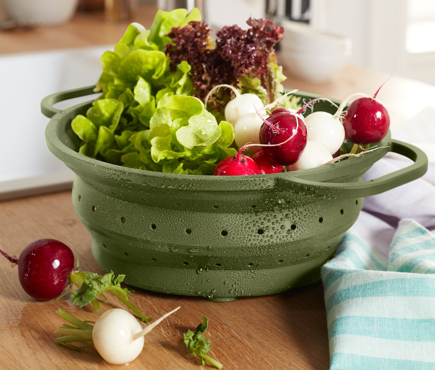 Ein grünes Platzspar-Sieb gefüllt mit Salat und Radieschen steht auf einer Holzoberfläche.