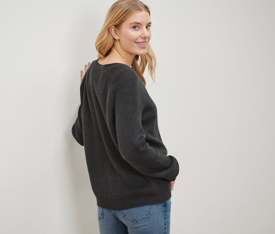 Blonde Frau blickt über ihre Schulter und trägt einen Grobstrick-Cardigan und Jeans.