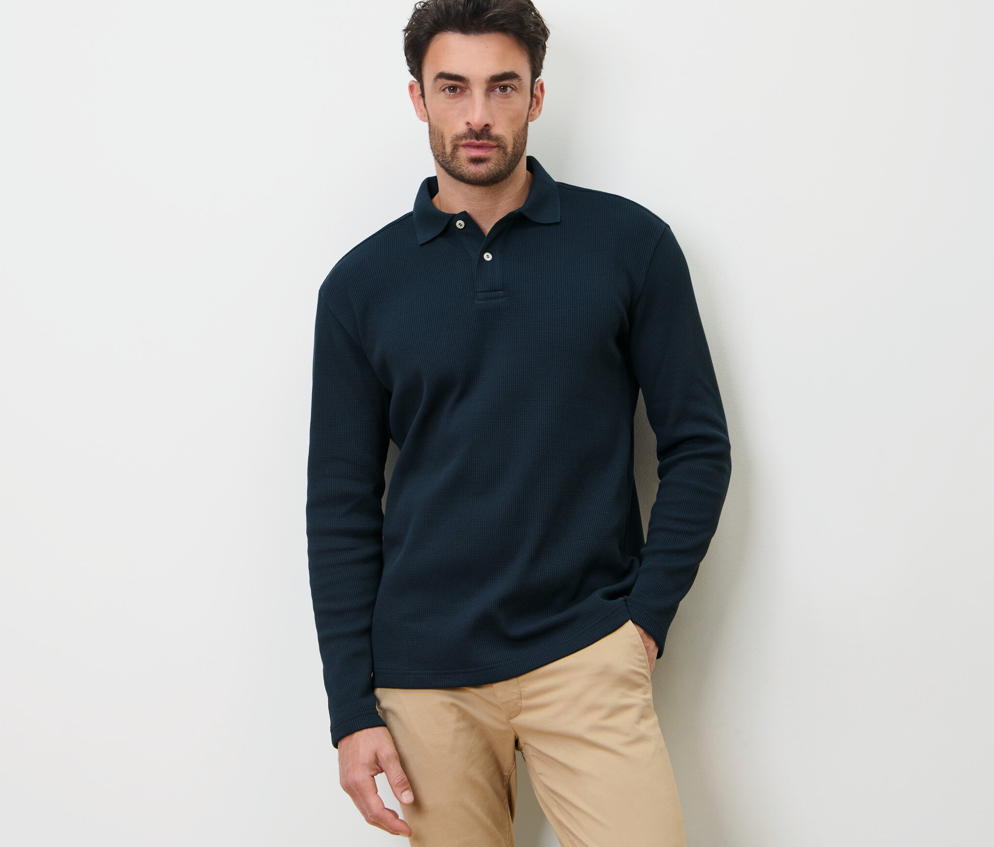 Ein Mann posiert vor einem weißen Hintergrund in einem dunkelblauen Langarm-Poloshirt.