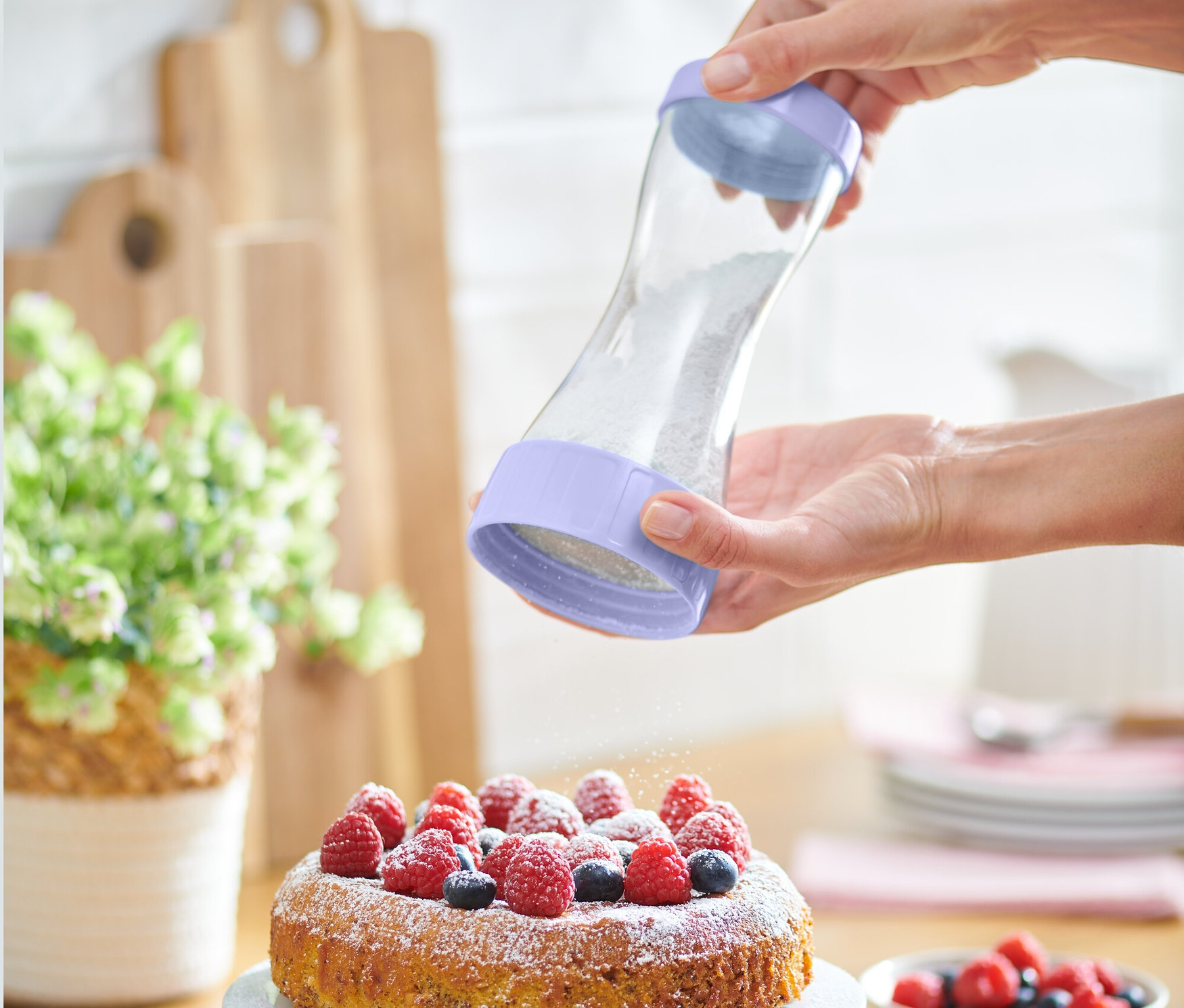 Eine Frau bestreut einen Kuchen mit Beeren mit einem Puderzuckerstreuer.