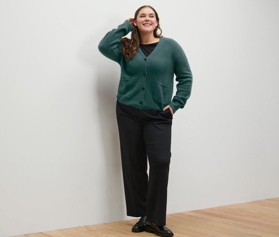 Frau posiert in dunkelgrüner Strickjacke mit Wolle und Komfort-Jerseyhose.