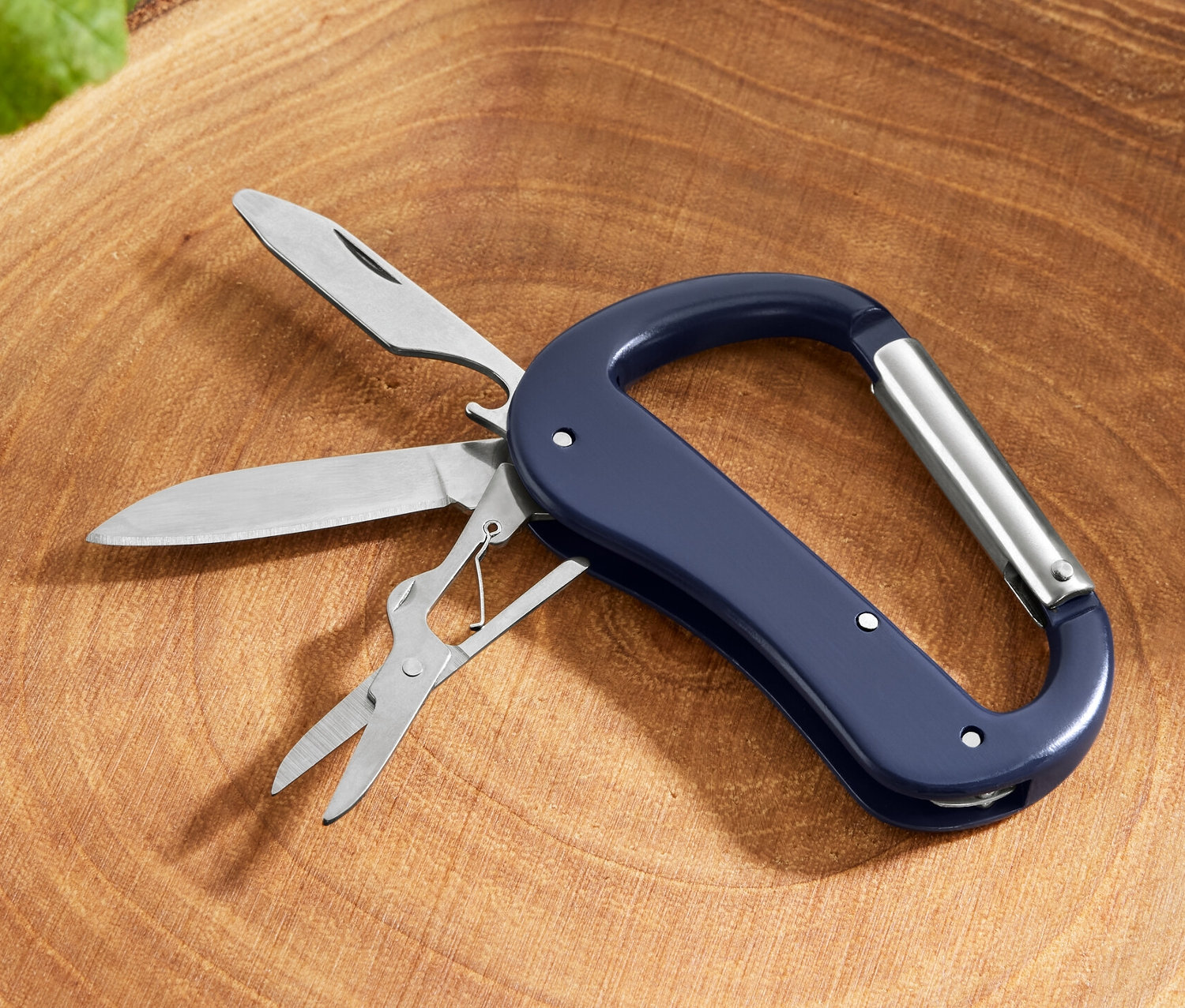 Ein 5-in-1-Karabiner-Multitool mit Messer, Säge und Schere liegt auf einem Baumstumpf.