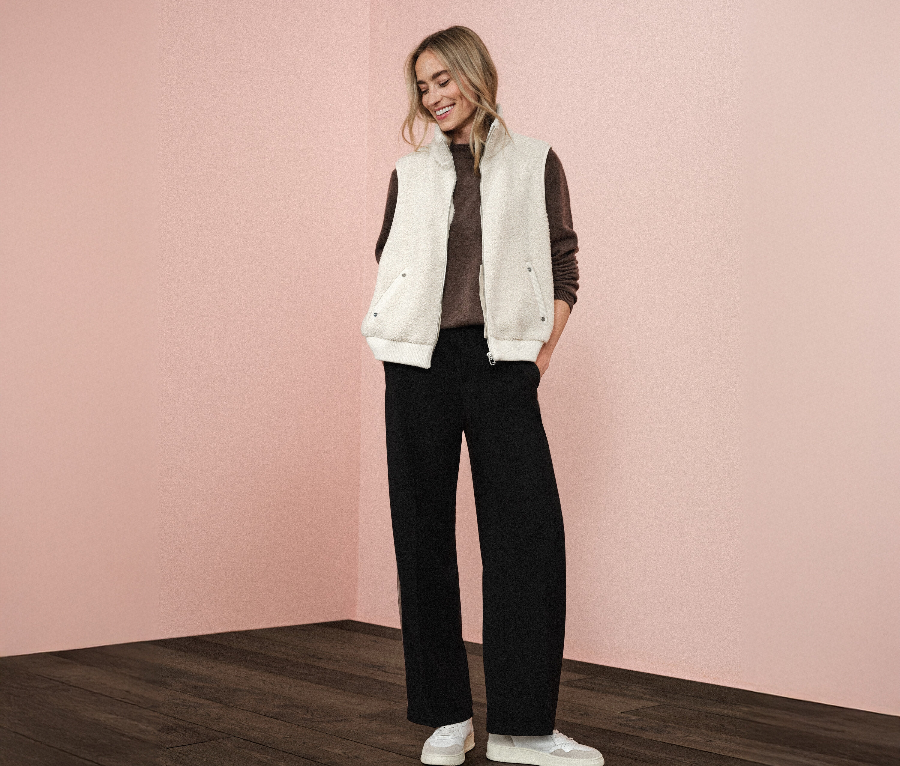 Frau trägt eine Street One Teddyweste über einem braunen Pullover, kombiniert mit einer schwarzen Hose und weißen Turnschuhen.
