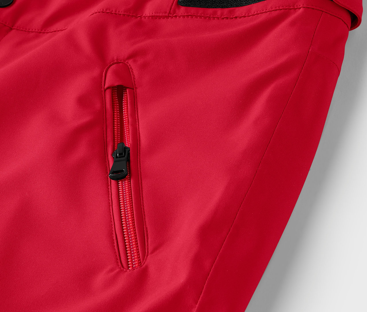 Detail einer roten Jacke mit schwarzem Taschenreißverschluss.