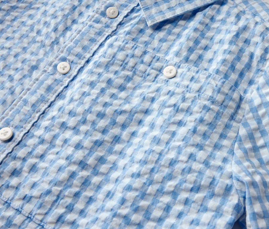 Detailansicht eines Kinderhemds mit blau-weißem Karomuster und Knöpfen.