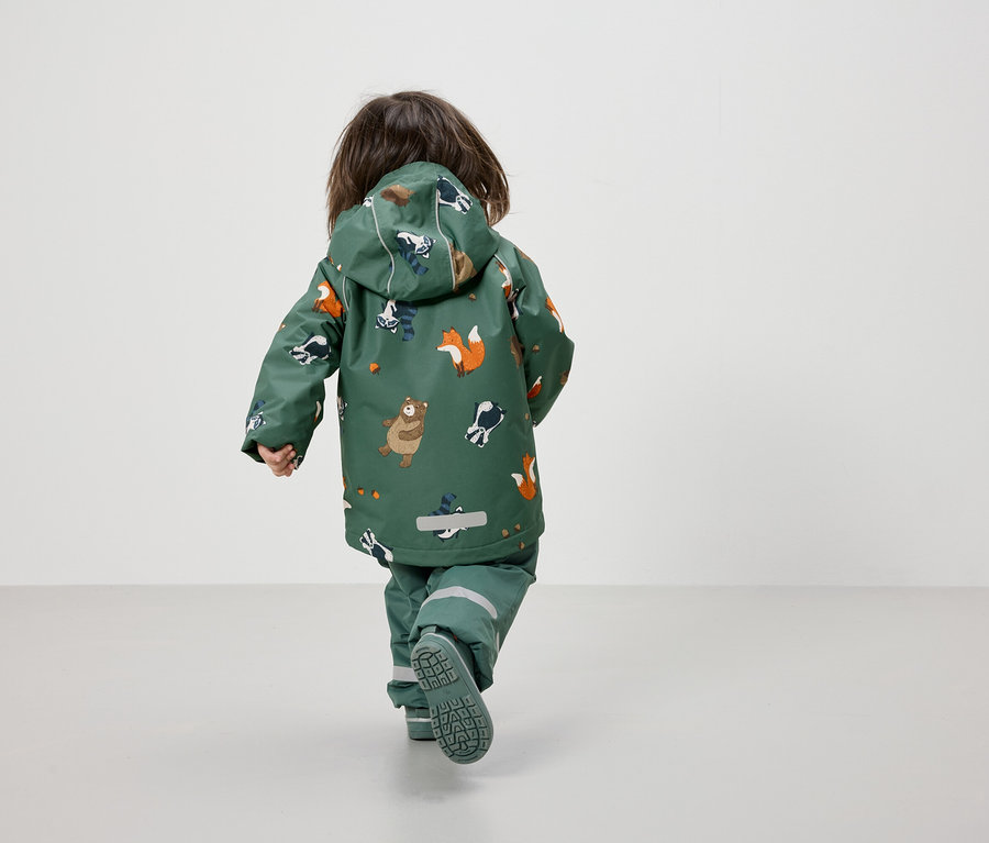 Kleinkind von hinten geht in einer grünen Jacke und Hose mit Tiermuster.