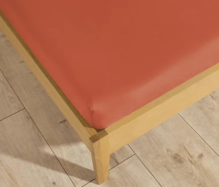 Detailaufnahme eines korallenfarbenen SCHÖNER WOHNEN-Kollektion Spannbetttuchs auf einem Bett.