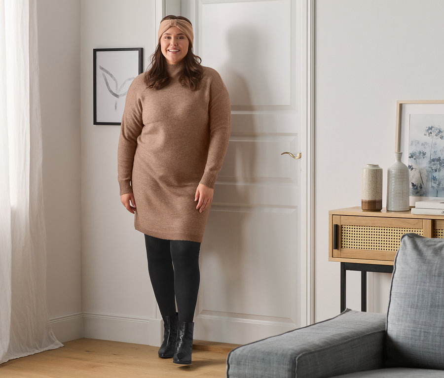 Frau posiert in einem Strickkleid und schwarzen Schuhen.