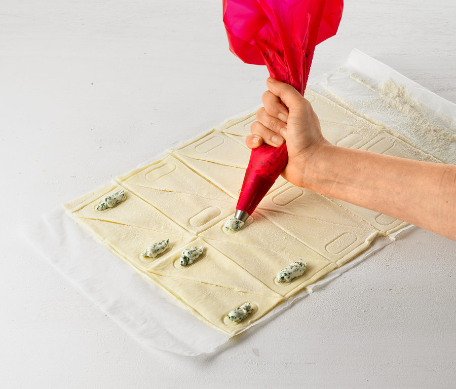 Eine Hand füllt mit einem Croissant-Roller Teig mit Füllung.